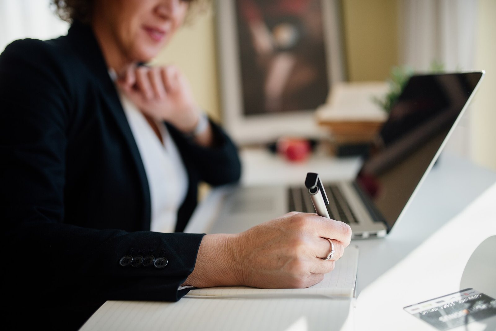 A person writing notes by hand next to an open laptop